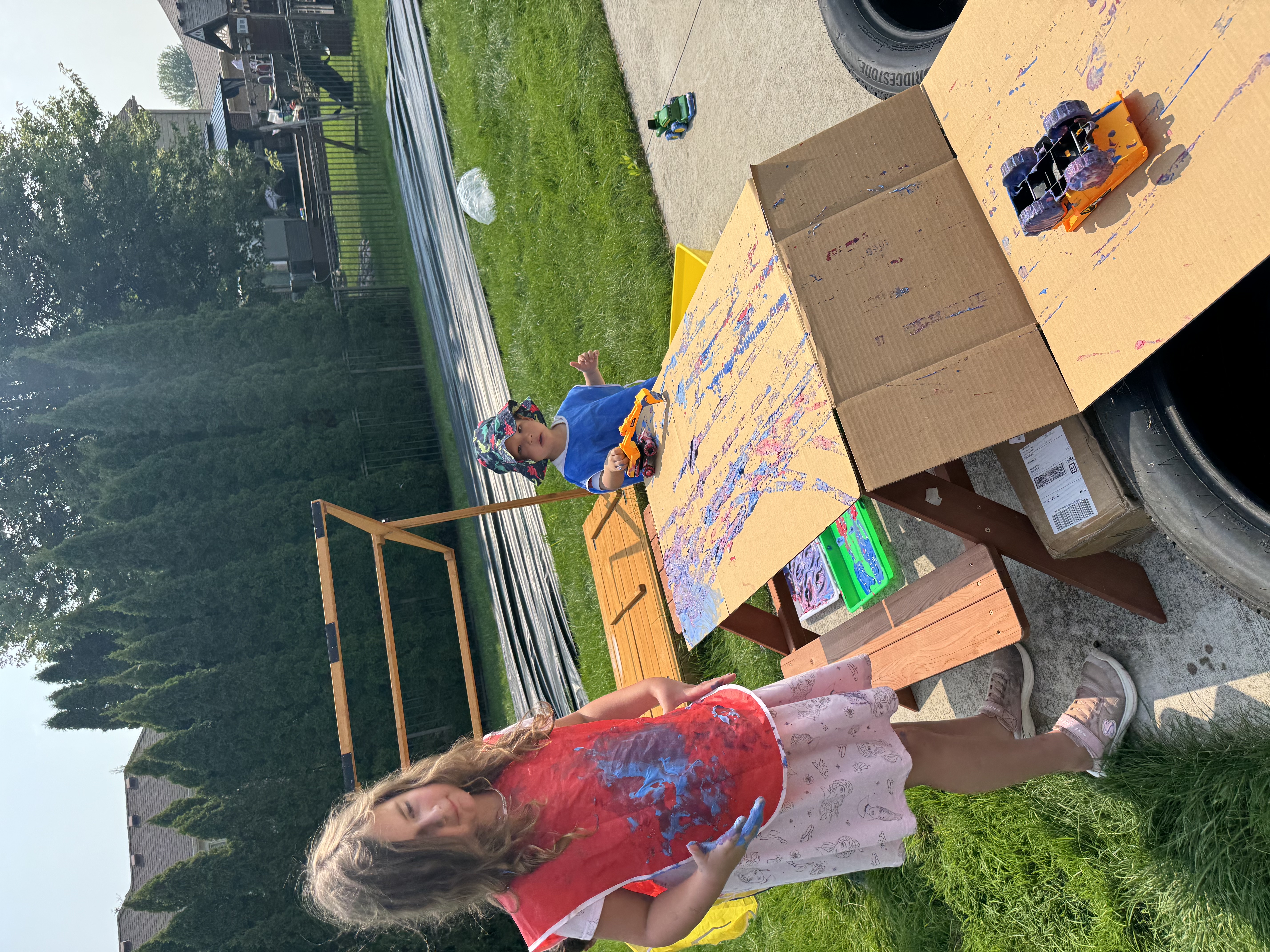 Children playing with paint, carboard, and toy cars