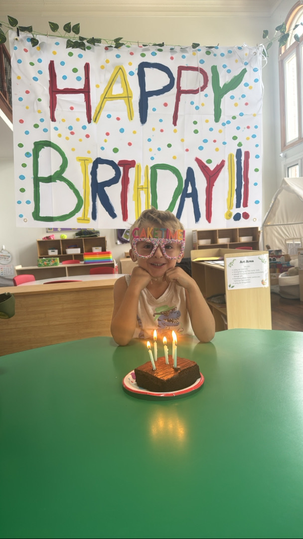 Child sitting in front of cake with candles and a happy birthday banner behind them