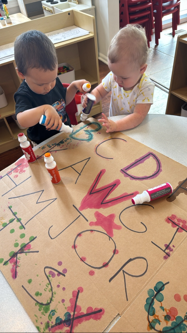 Childen playing with markers on cardboard with alphabet labeled on it
